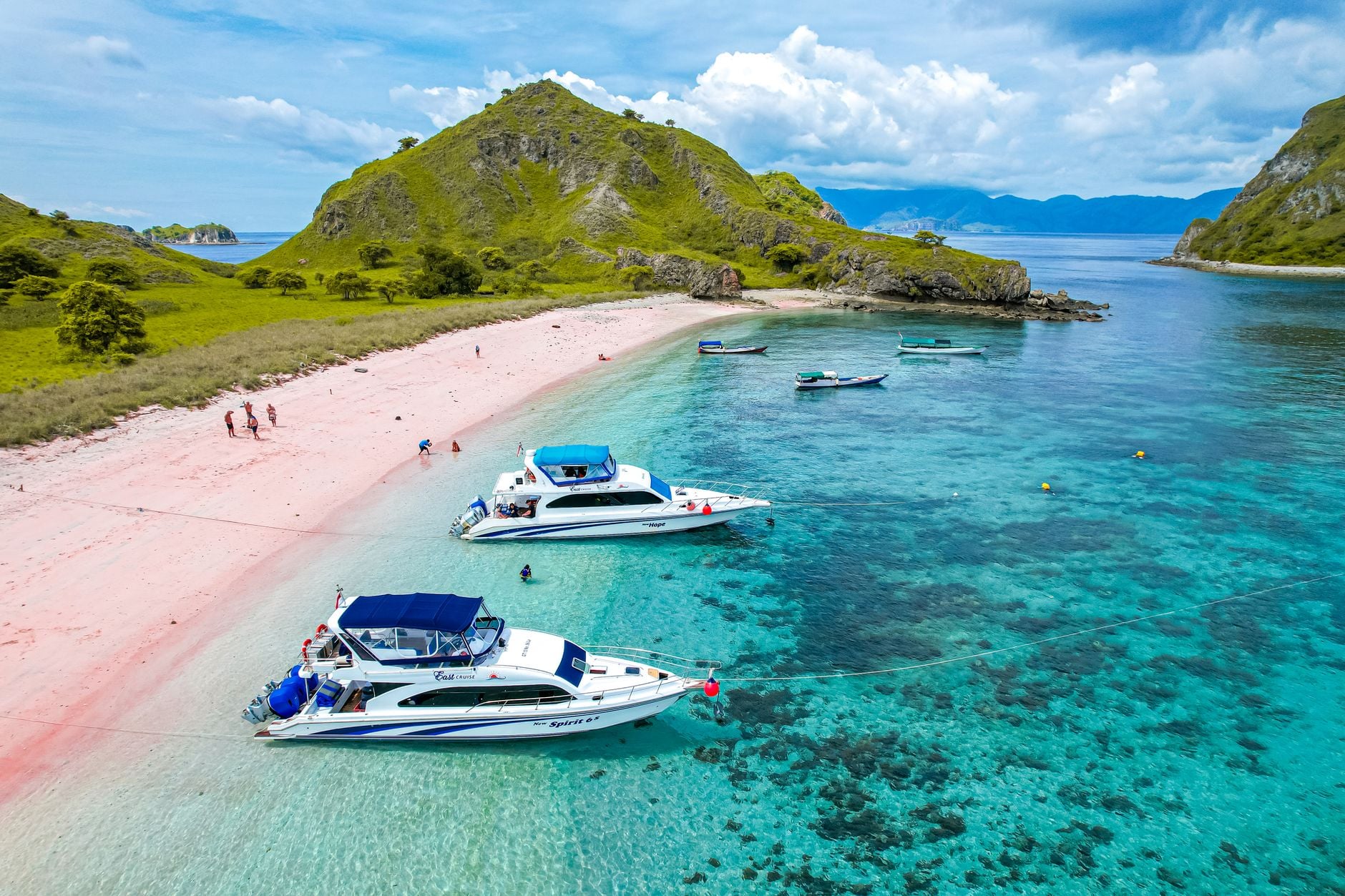 Aerial view of multiple tourist boats moored at Pink Beach, Komodo National Park, with pink sand and turquoise water visible
