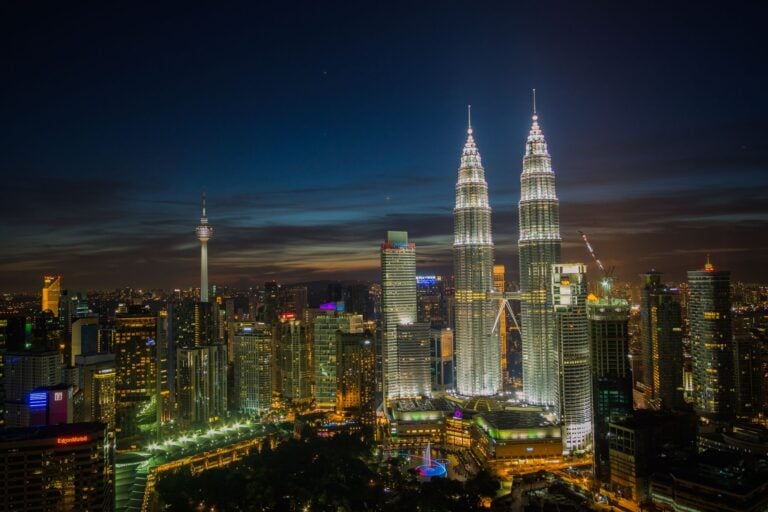Die Skyline von Kuala Lumpur in der Abenddämmerung mit den Petronas Twin Towers und dem KL Tower, die sich vor blauem Himmel abheben