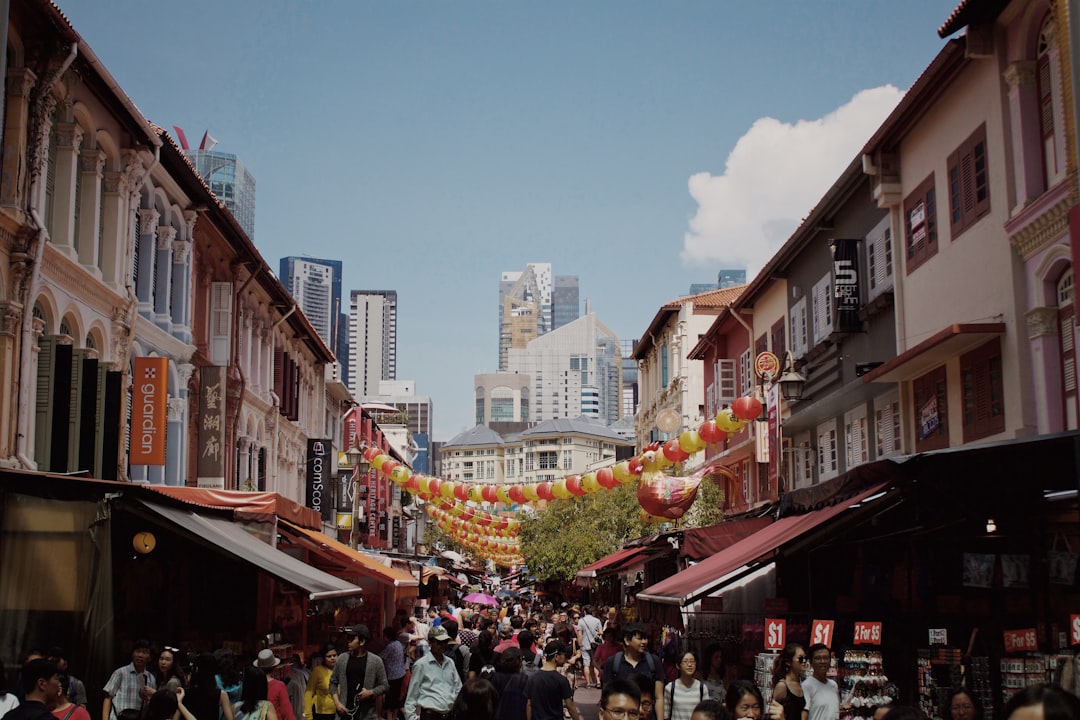 Crowded Singapore Chinatown street with red lanterns strung between shophouses and skyscrapers in the background