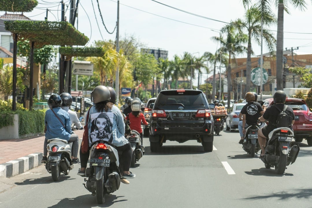 Busy Bali road with scooters, motorcycles, and cars under palm trees on a sunny day