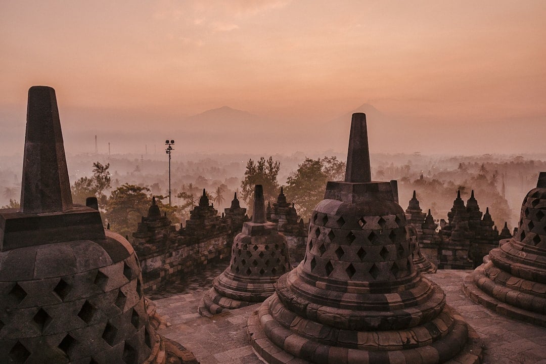 Borobudur temple stupas glowing in warm pink and orange light at sunrise with volcanic mountains and mist in the background, Java, Indonesia