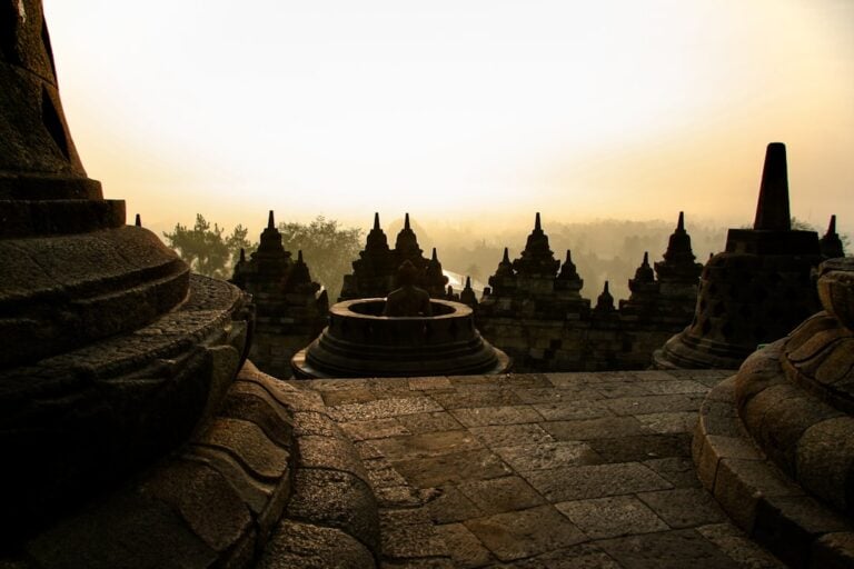 Borobudur temple stupas silhouetted against a golden sunrise sky with morning mist, Java, Indonesia