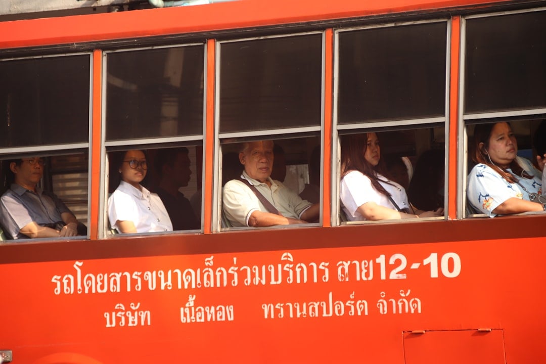 Passeggeri seduti all'interno di un autobus pubblico rosso di Bangkok con scritte in lingua thailandese sul lato.