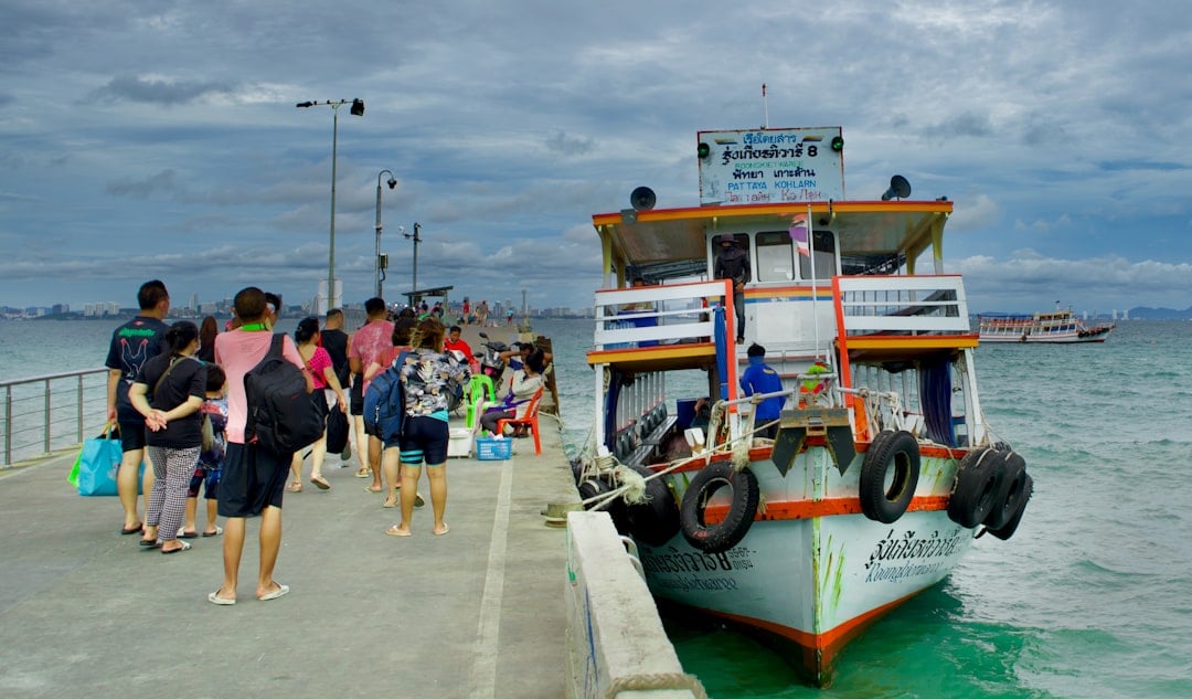 Passeggeri in coda per imbarcarsi su un piccolo traghetto thailandese a un molo, con il mare turchese sullo sfondo.