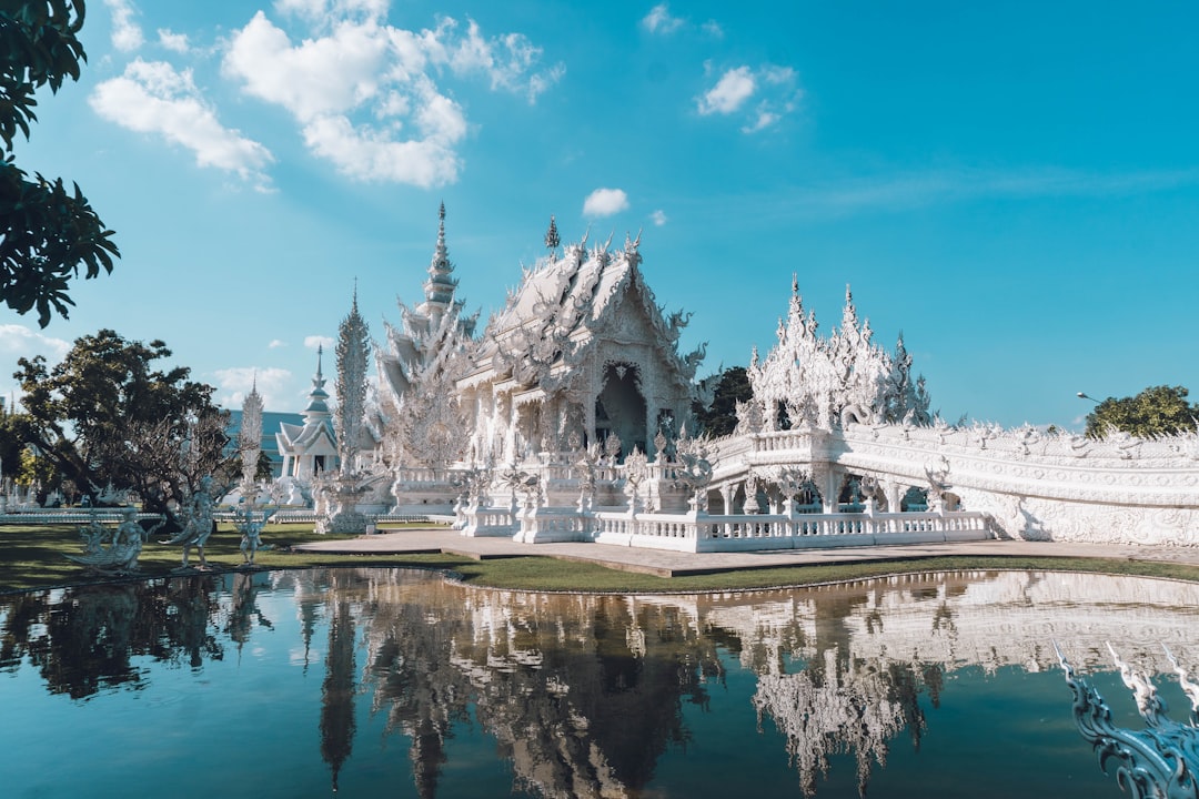 Wat Rong Khun, Kuil Putih di Chiang Rai, Thailand, tercermin di kolam di bawah langit biru cerah dengan menara-menara berornamen putih yang berkilauan di bawah sinar matahari