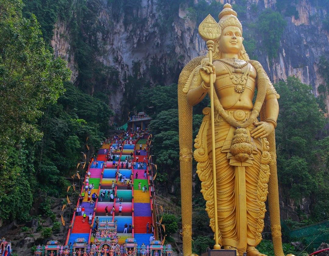 The towering golden Lord Murugan statue at the entrance to Batu Caves, with the colourful staircase and limestone cliffs behind