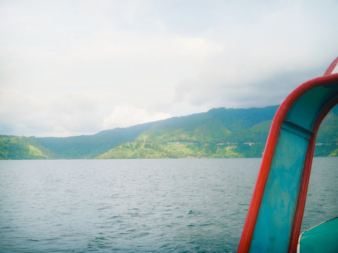 View from inside a passenger ferry crossing Lake Toba toward the green crater rim hills of Samosir Island, North Sumatra