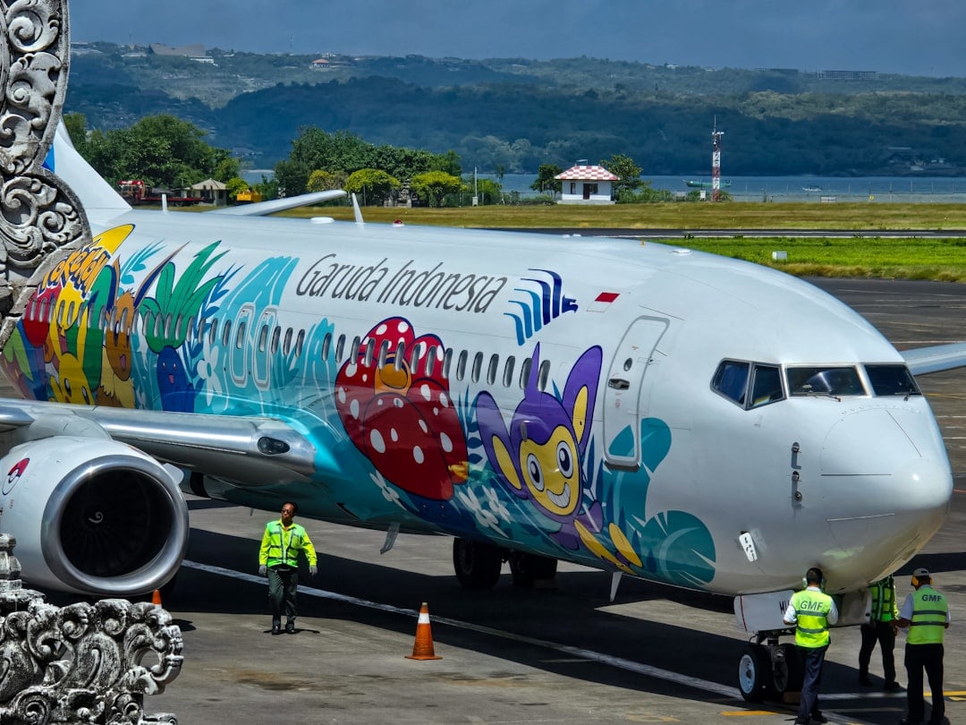A Garuda Indonesia aircraft with colourful livery on the tarmac at Ngurah Rai International Airport in Bali, with green hills and water in the background