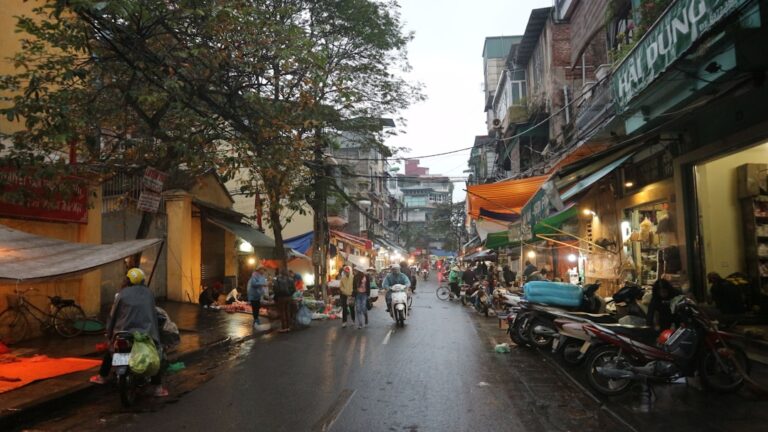 Straßenszene im Altstadtviertel von Hanoi in der Abenddämmerung mit Motorbikeund Marktstände säumten eine nasse Straße