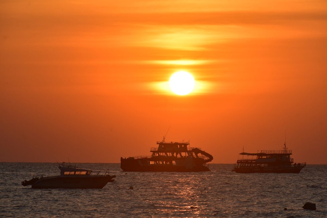 Silhouettes of cruise boats on the sea against a vivid orange and red sunset sky in Thailand