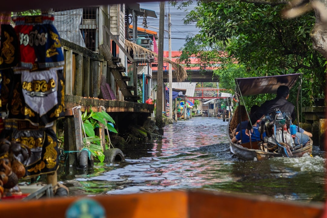 Long-tail boat navigating a narrow Bangkok canal past traditional wooden houses on stilts