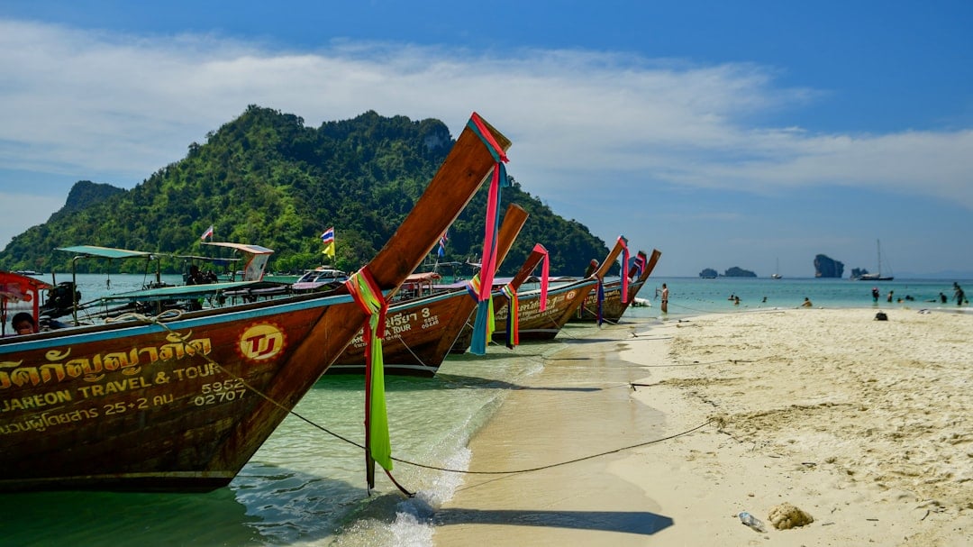 Traditional Thai longtail boats lined up on a white sand beach in the Phi Phi Islands with limestone cliffs in the background