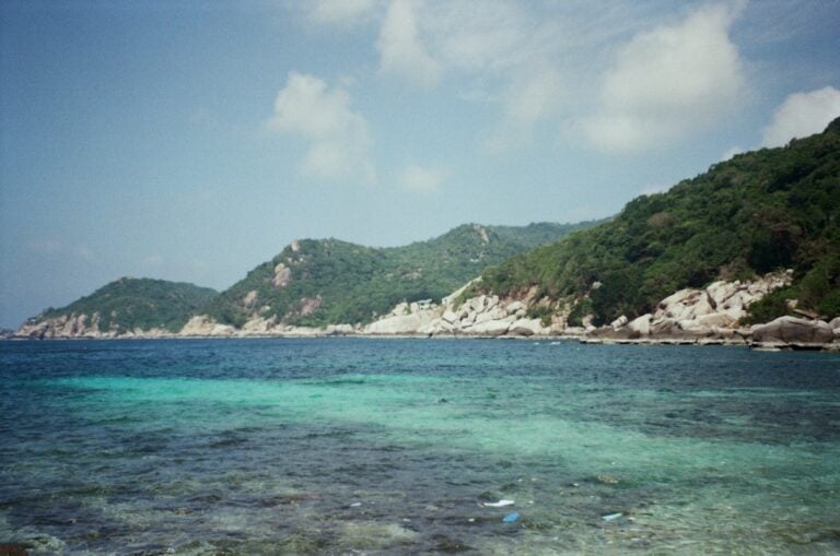 Acque turchesi e costa rocciosa ricoperta di giungla di un'isola tropicale thailandese, simile a Koh Chang.