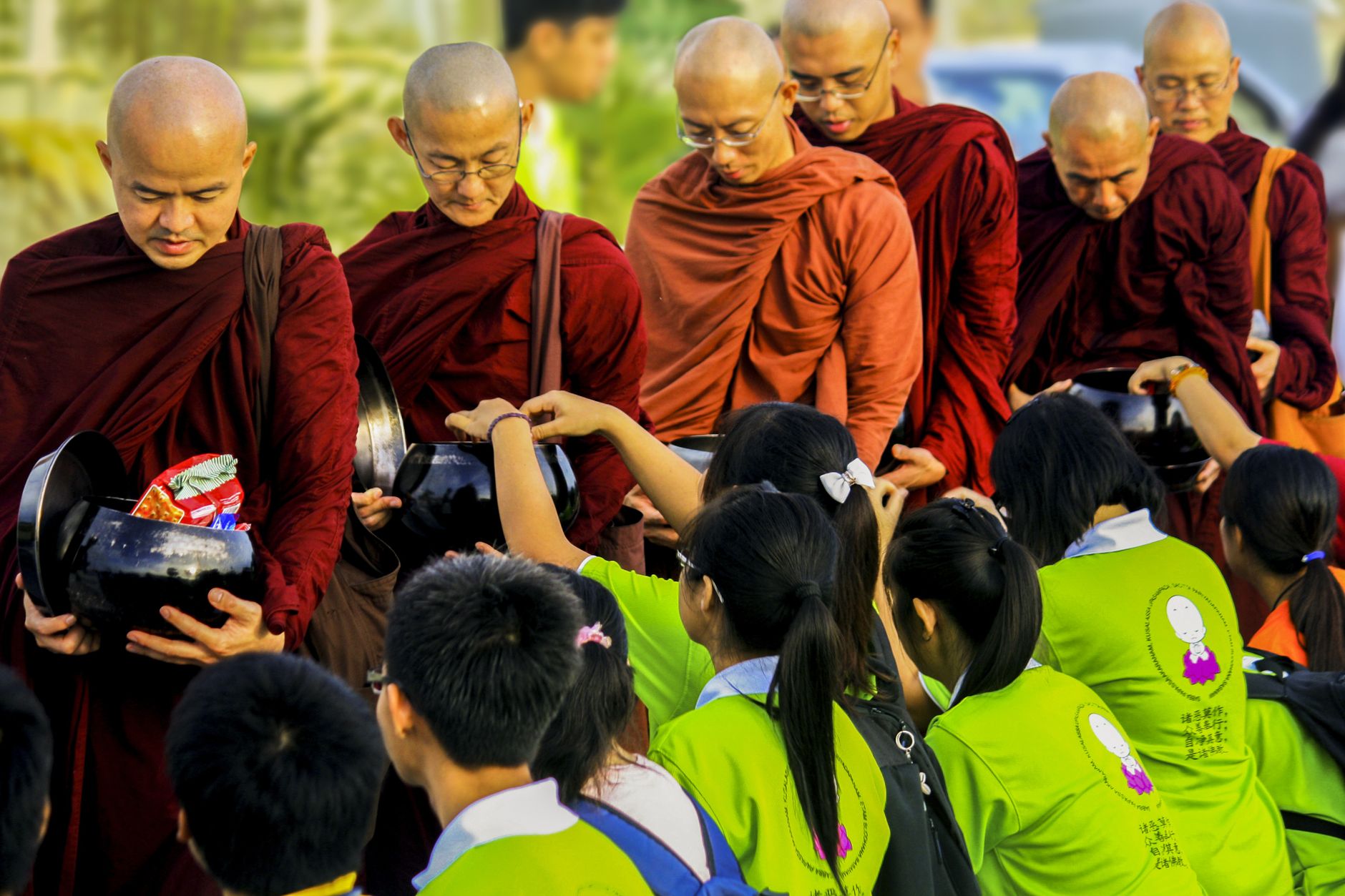 Buddhist monks in saffron robes receiving food offerings from devotees during an alms-giving ceremony