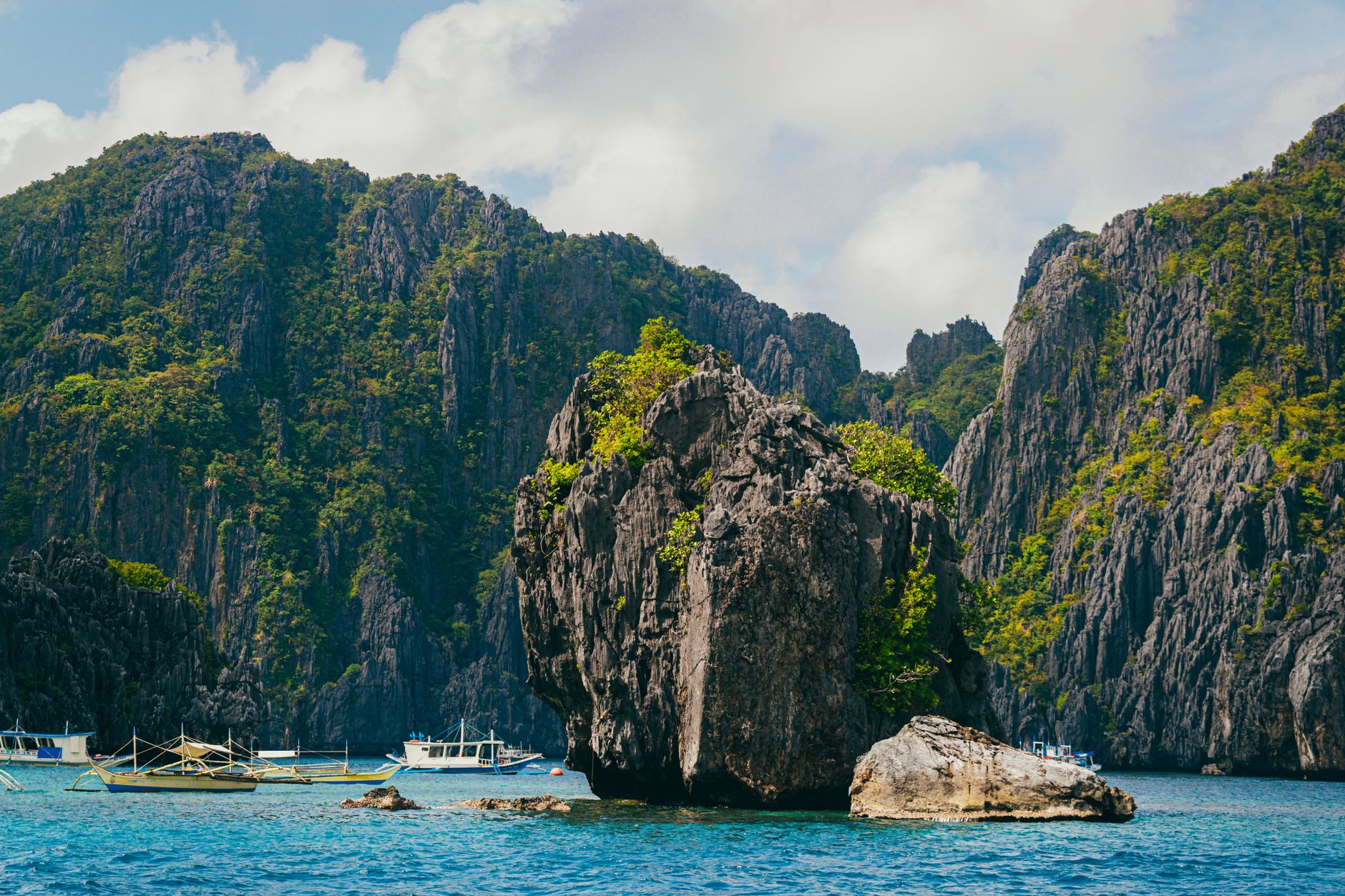 Dramatic limestone karst cliffs rising from turquoise water with traditional bangka boats anchored below in El Nido, Palawan, Philippines