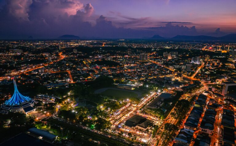 Aerial night view of Kuching, Sarawak, Malaysia, showing city lights and landmarks from above.