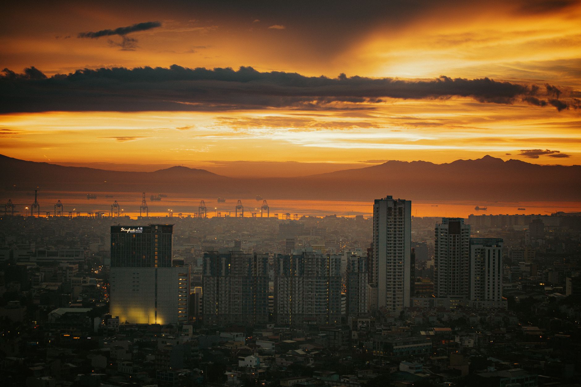 Manila cityscape at sunset with a dramatic orange and golden sky over the bay and mountains in the background