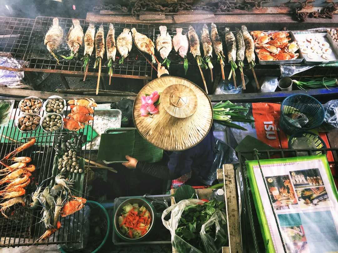 Overhead view of a Thai seafood night market stall with grilled fish, prawns, and crab, tended by a vendor in a conical hat