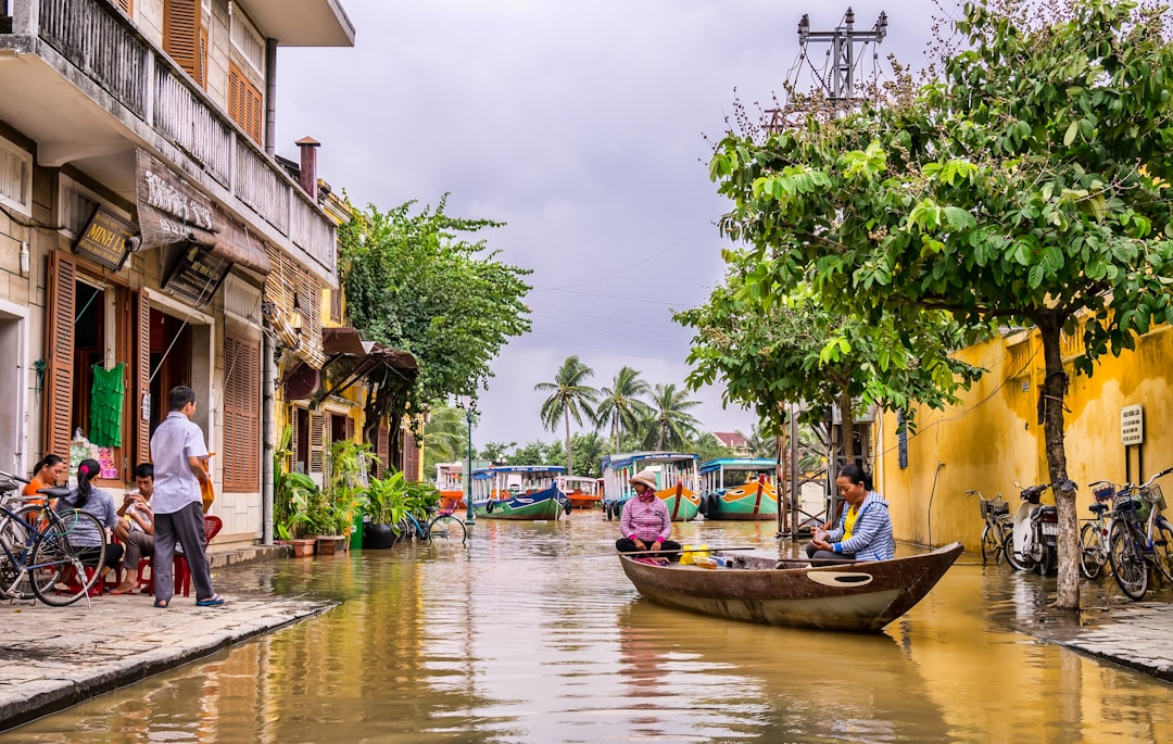 Flooded street in Hoi An old town during wet season with locals navigating by boat past yellow shophouses
