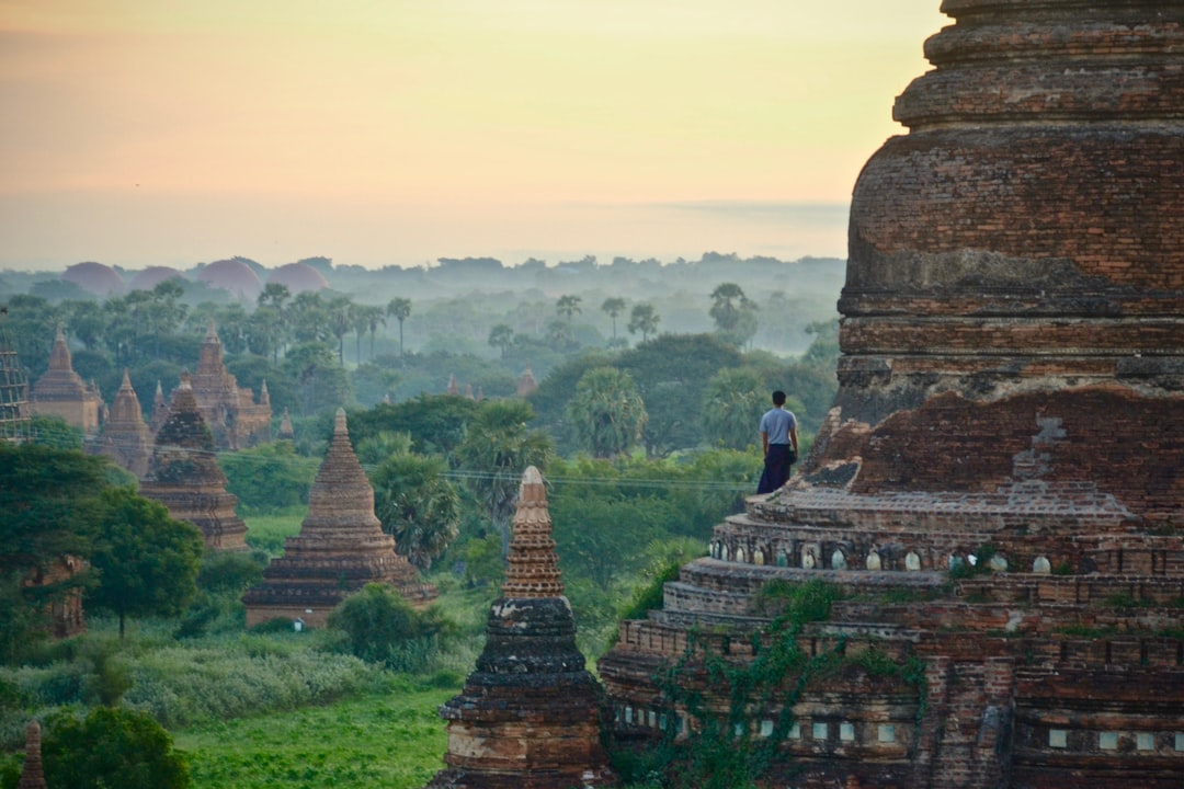 Traveller standing on a Bagan temple watching sunrise over the misty temple plain, Myanmar