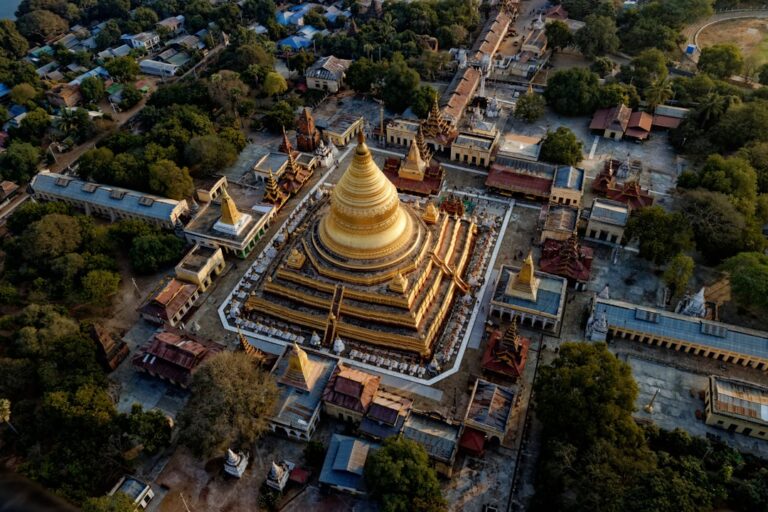 Aerial view of a golden pagoda complex in Myanmar, surrounded by trees and smaller shrines. Photo by Unsplash.
