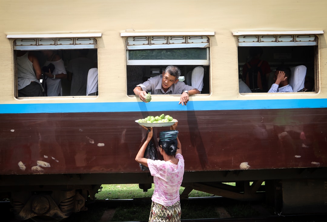 A vendor passes fruit up through a Myanmar train window to a passenger leaning out — a typical scene on the Yangon Circular Railway.