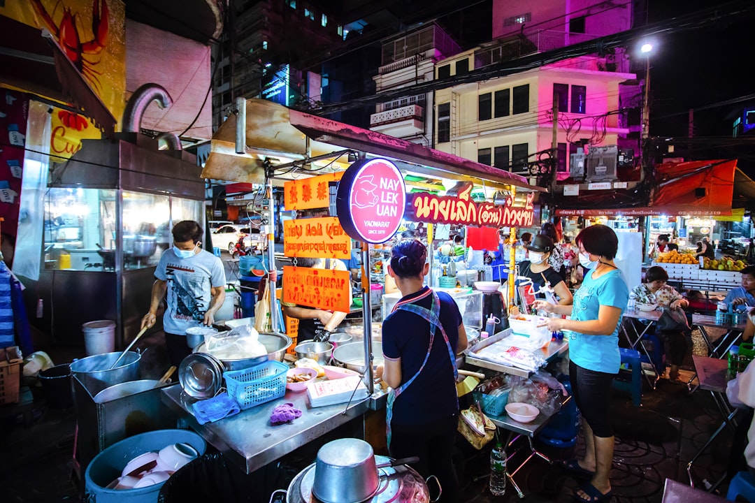 Nay Lek Uan street food stall in Bangkok's Chinatown at night, with cooks working over steaming pots and crowds gathered around plastic tables