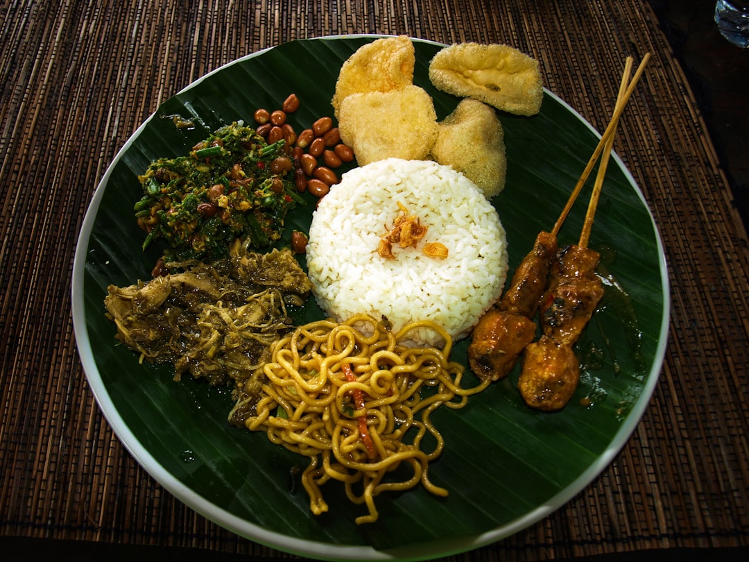 A traditional Indonesian nasi campur plate served on a banana leaf with rice, satay skewers, vegetables, peanuts and crackers at a Bali warung