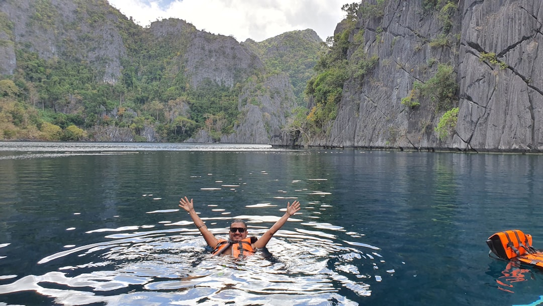 A swimmer floating in calm turquoise water enclosed by dramatic grey limestone cliffs in Coron, Palawan, Philippines