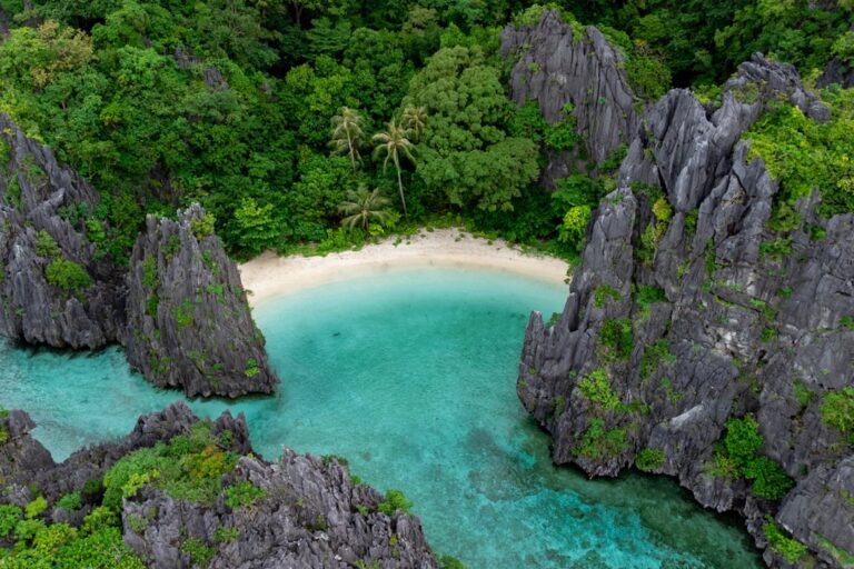 Aerial view of El Nido's Secret Beach in Palawan, Philippines, surrounded by jagged limestone cliffs with turquoise water and white sand