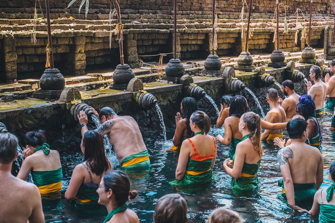 Balinese Hindus in green and yellow sarongs performing the melukat purification ritual at the sacred water spouts of Tirta Empul temple near Ubud, Bali