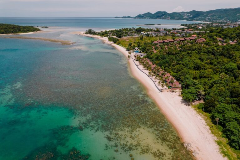 Aerial view of Koh Samui island coastline with turquoise water, white sand beach, and lush green hills, Thailand