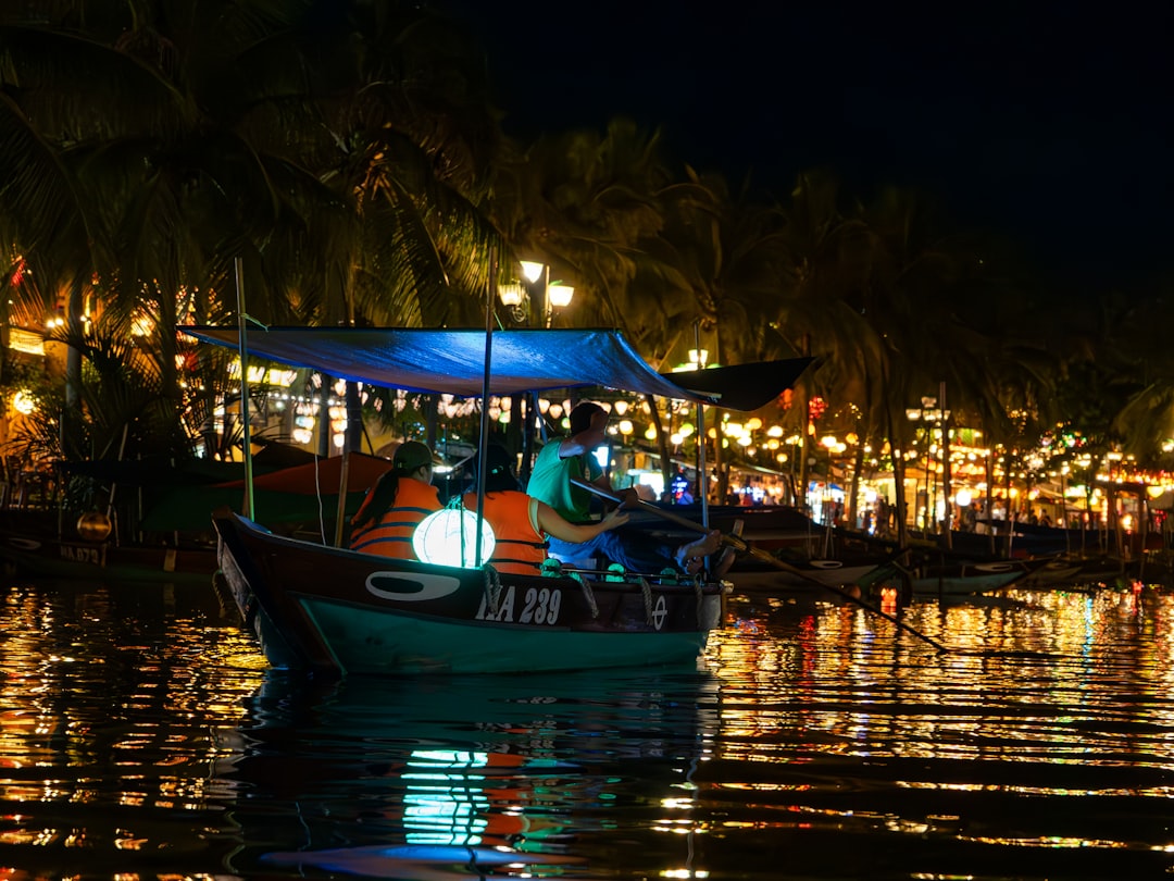 Traditional wooden boat on the Thu Bon River at night in Hoi An, surrounded by glowing lanterns and colorful reflections on the water