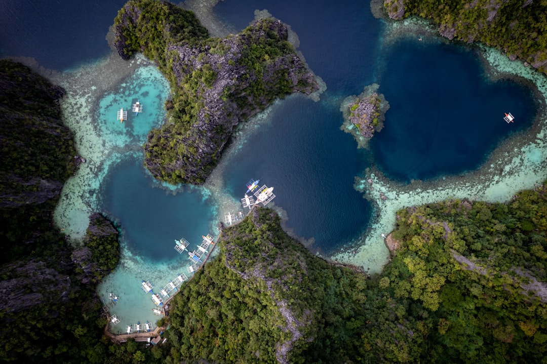 Aerial view of island-hopping boats docked in a lagoon surrounded by limestone islands and turquoise water, Palawan Philippines