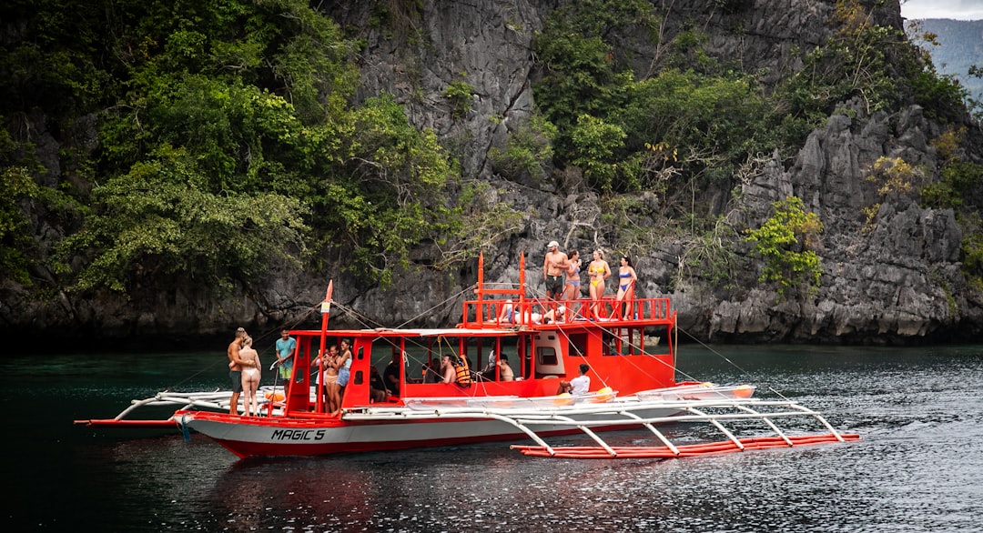 Tourists on a traditional red bangka boat beside towering limestone cliffs in El Nido, Palawan during an island hopping tour