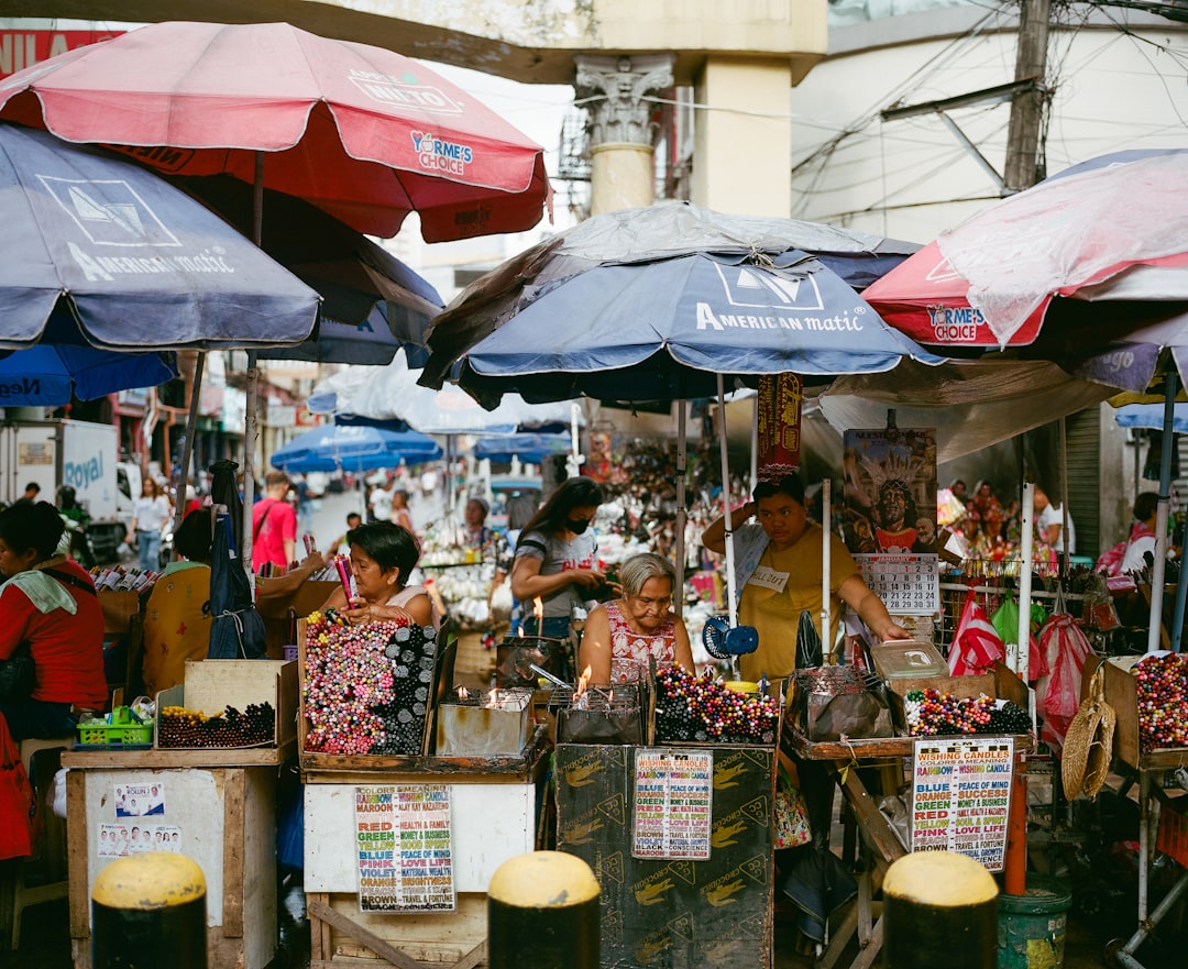 Busy outdoor Filipino market with vendors selling produce under colorful umbrellas