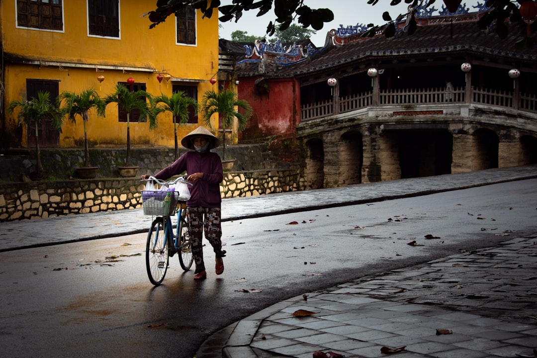 A local woman pushes her bicycle past the Japanese Covered Bridge in Hoi An's Ancient Town, Vietnam