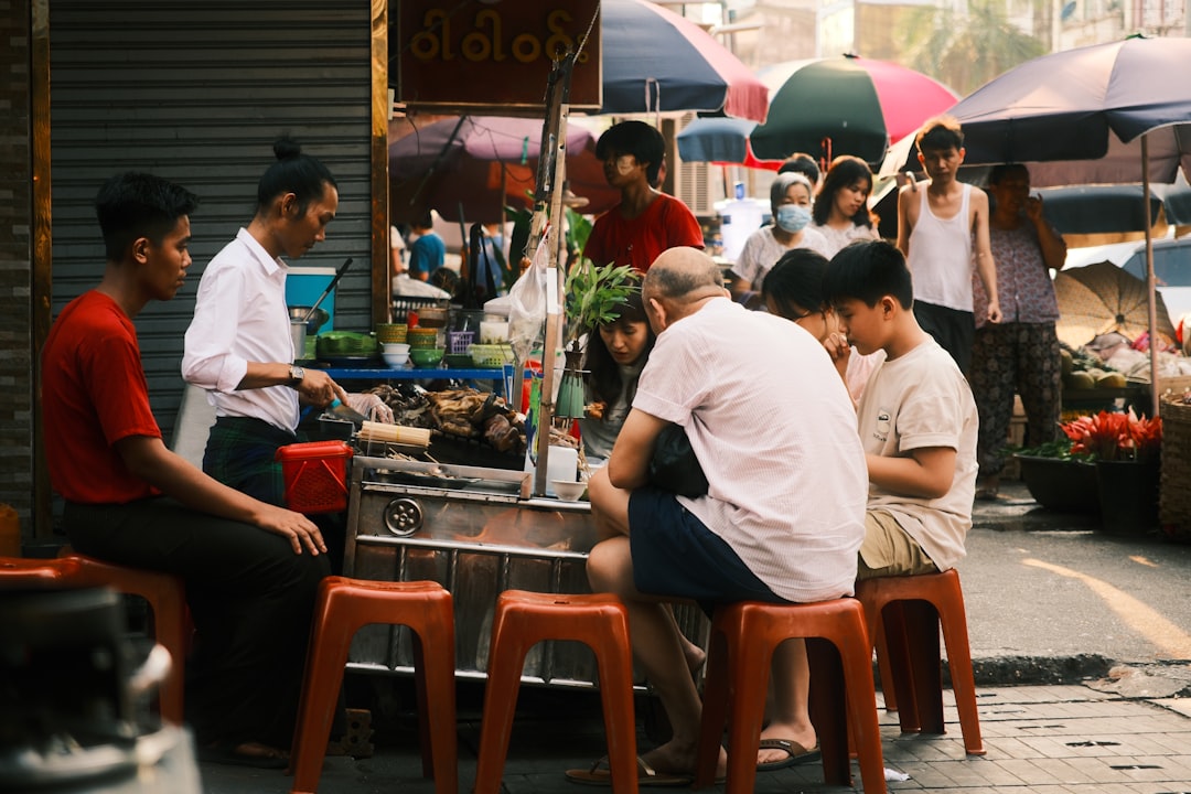 People sitting on red plastic stools eating at an outdoor street food stall on 17th Street in Yangon, Myanmar.