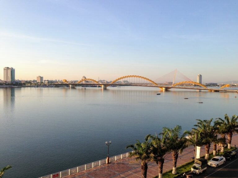 Da Nang's Dragon Bridge arching over the Han River at golden hour, with palm trees lining the riverfront promenade